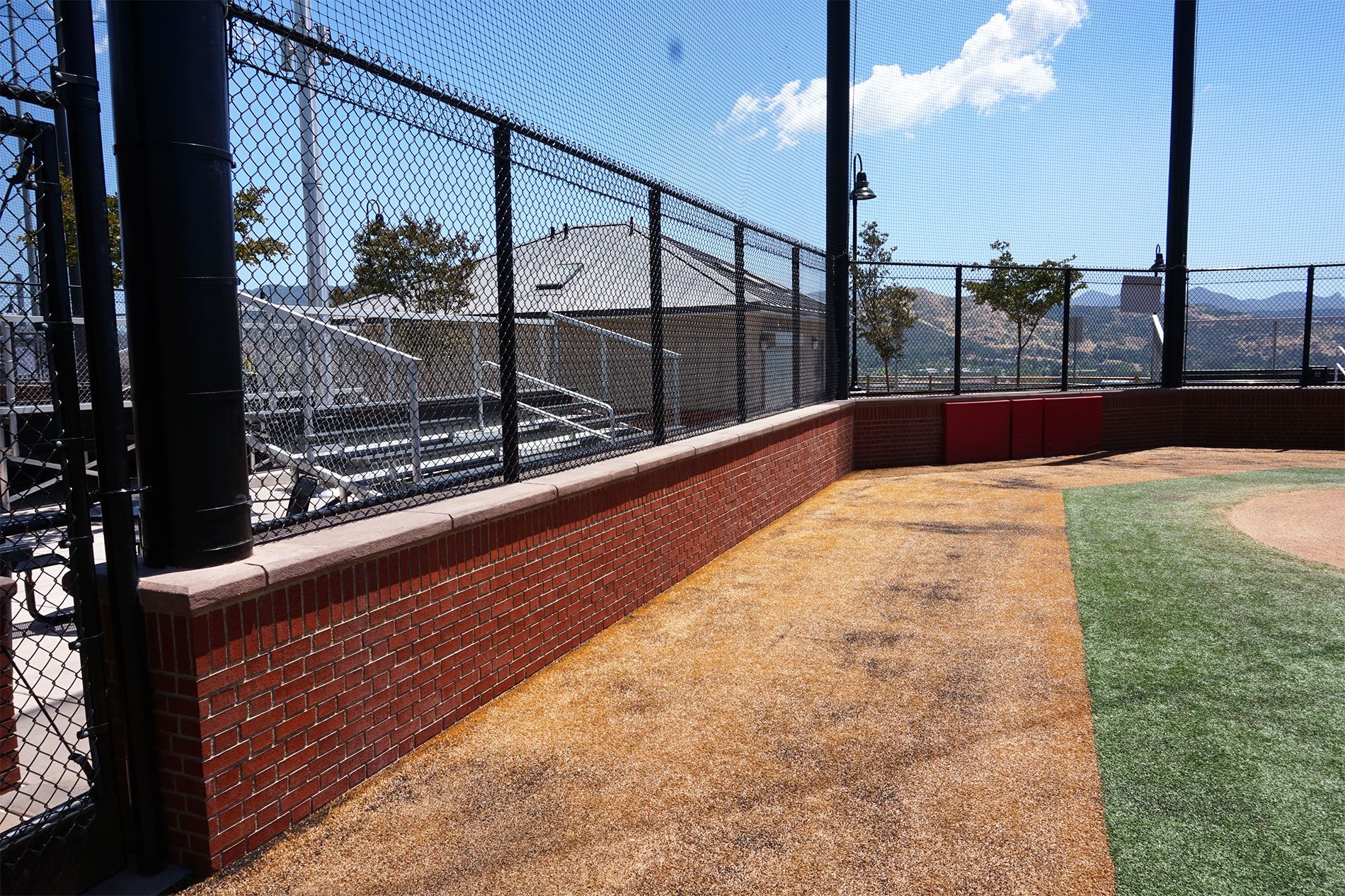 Red brick backstop wall with chain-link fencing behind home plate at the Triunfo YMCA baseball fields