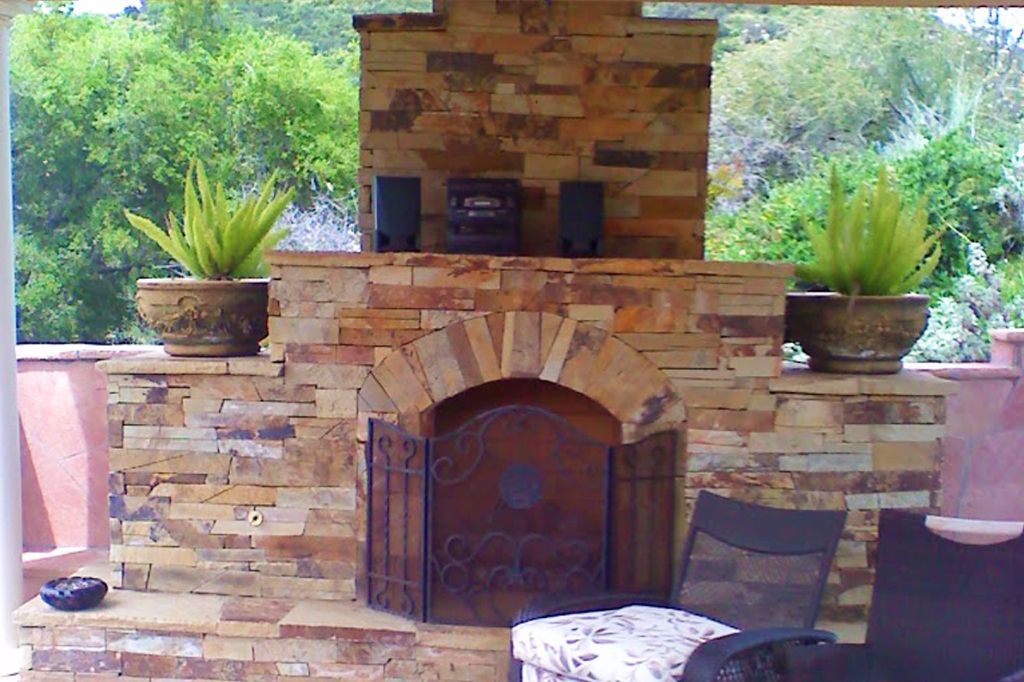 Tall stacked-stone outdoor fireplace with an arched firebox and raised hearth on a backyard patio