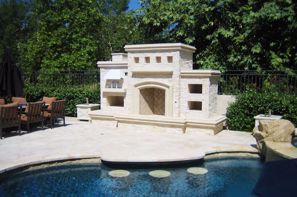 Cream cast stone fireplace and chimney standing beside a swimming pool