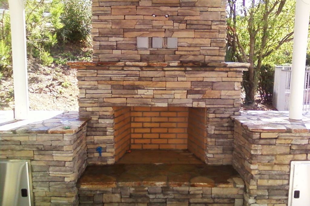 Stone and brick outdoor fireplace with a timber mantel under a covered patio