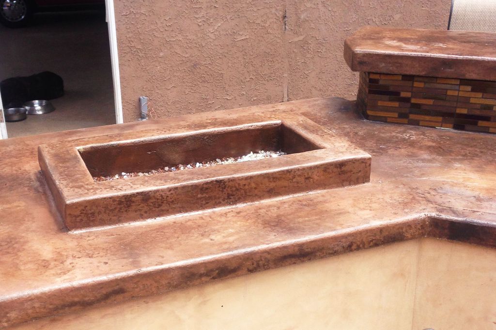 Close on the cast fire trough and the counter returns, copper-stained concrete over a tiled base