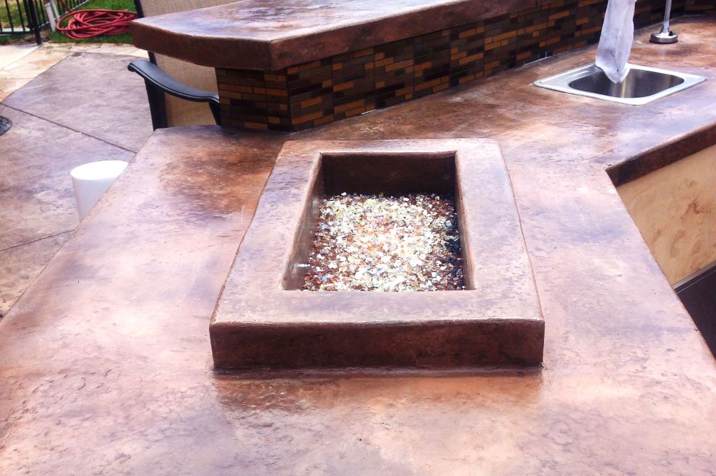 Backyard concrete counter with a fire trough cast into it and filled with fire glass, raised bar top behind