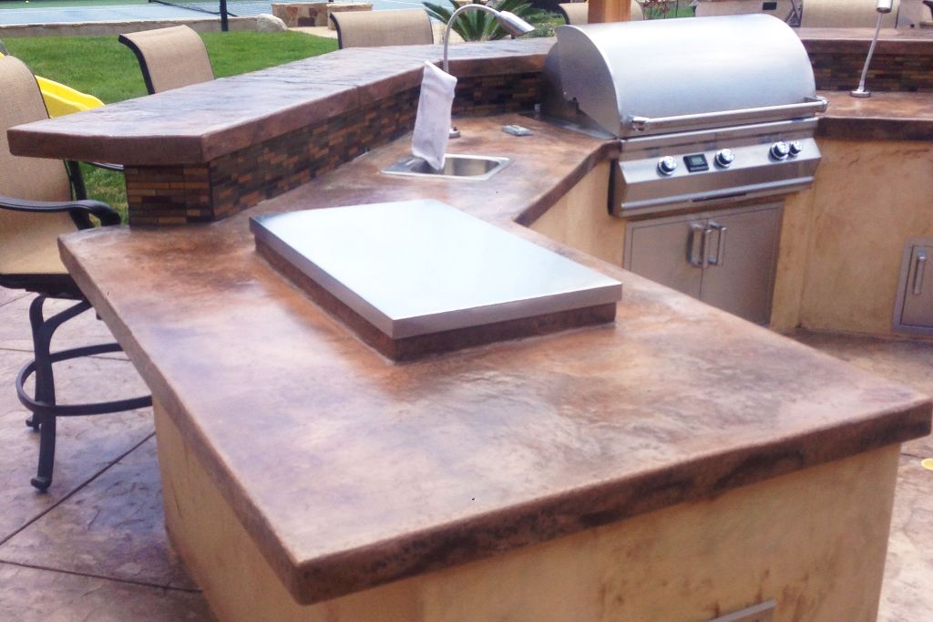L-shaped backyard kitchen counter in acid-stained concrete with an integrated sink, built-in grill and bar seating