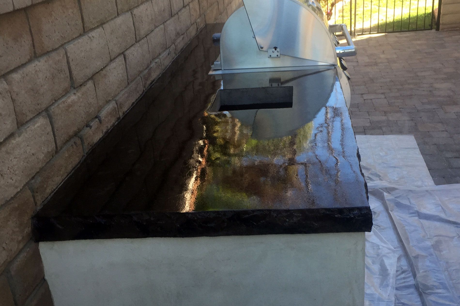 The same black concrete counter carried past a built-in stainless barbecue, block wall and paver patio behind