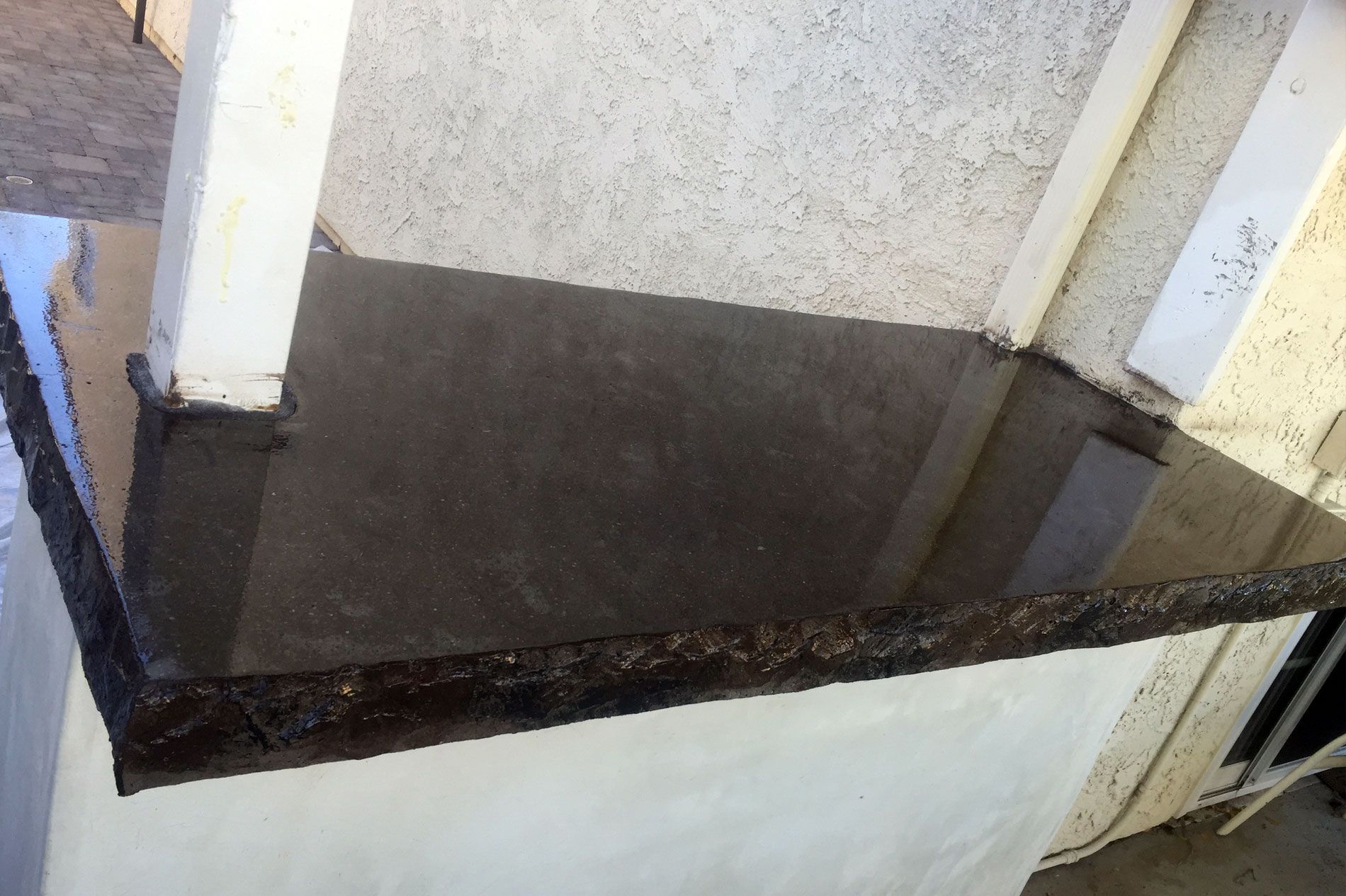 Black cast concrete countertop with a hand-chiseled rock-face edge, running along a stucco wall