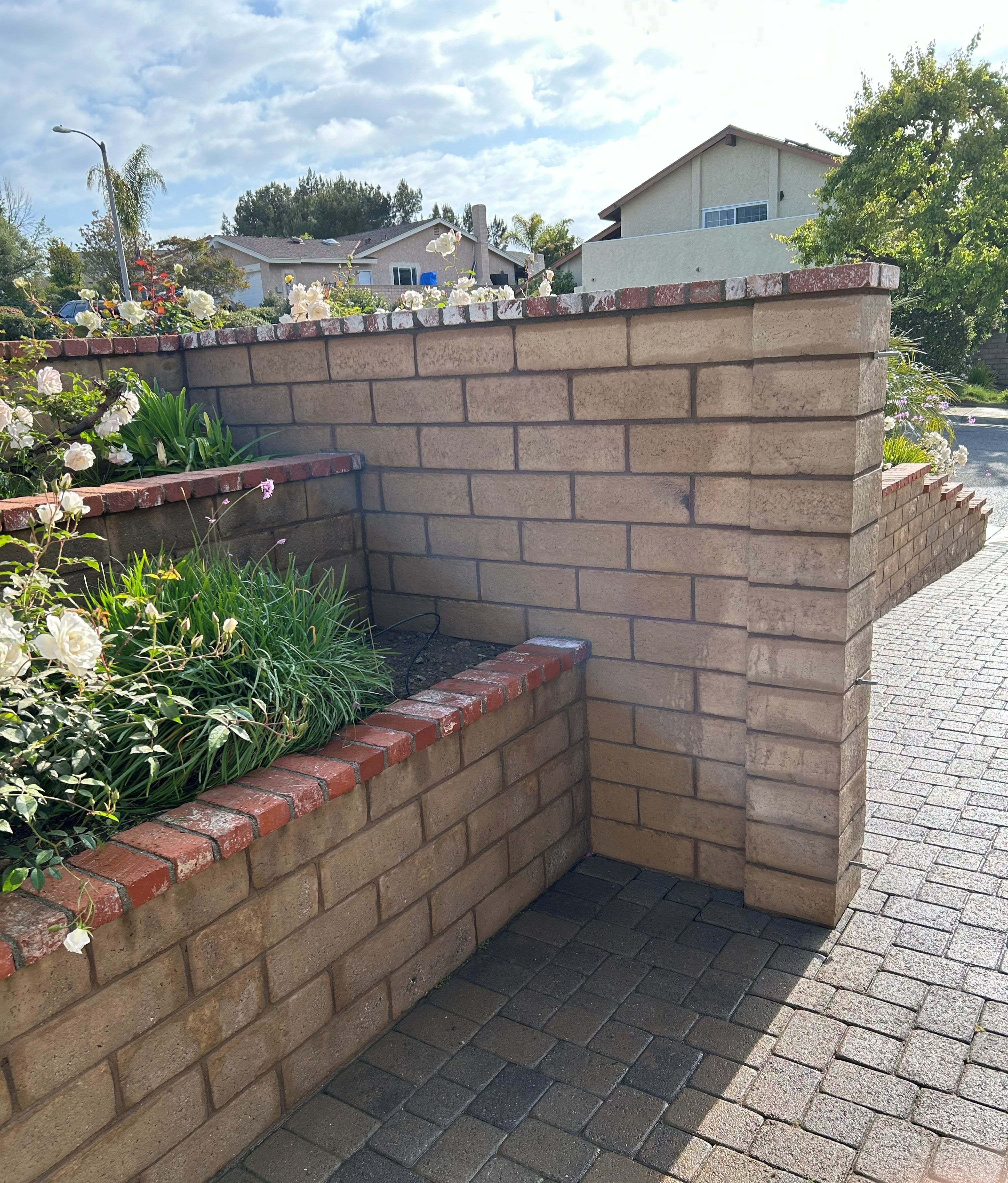 Block retaining wall with a brick cap turning the corner alongside a paver driveway
