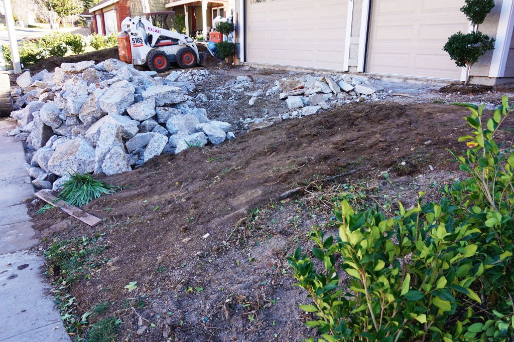 Broken-out concrete stacked for removal on a stripped driveway