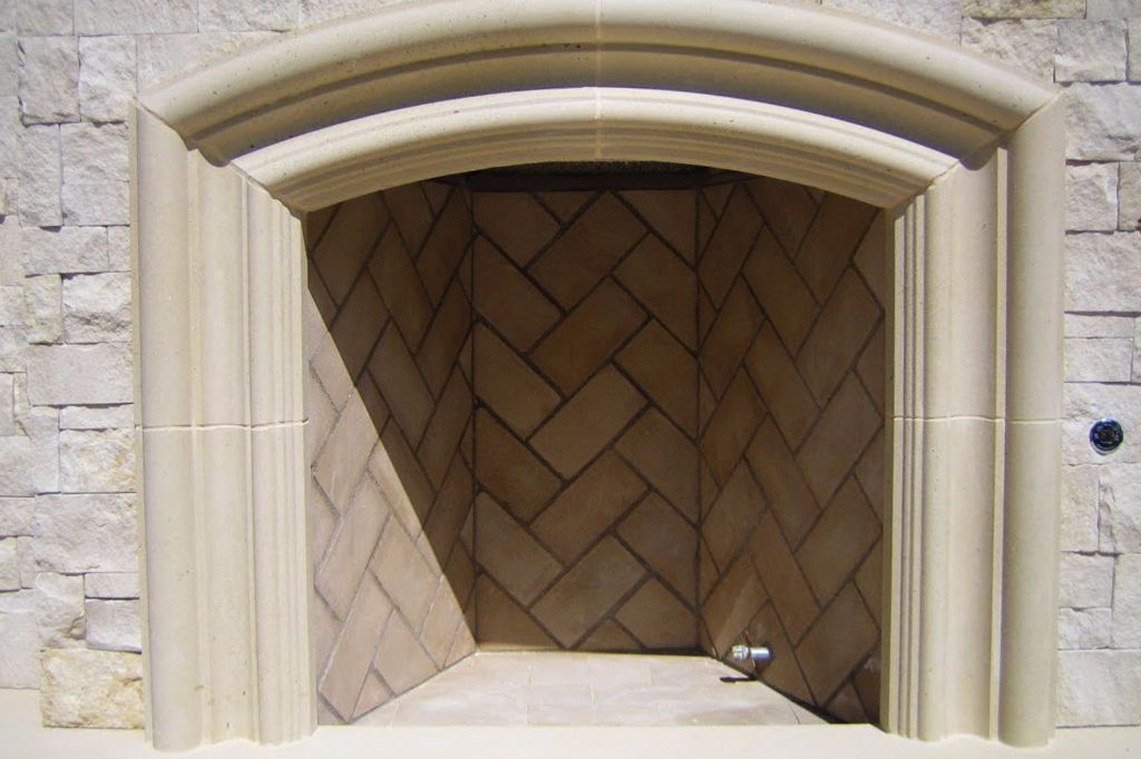 Close on a cast stone fireplace surround, the moulded arch and fluted jambs framing a herringbone firebox