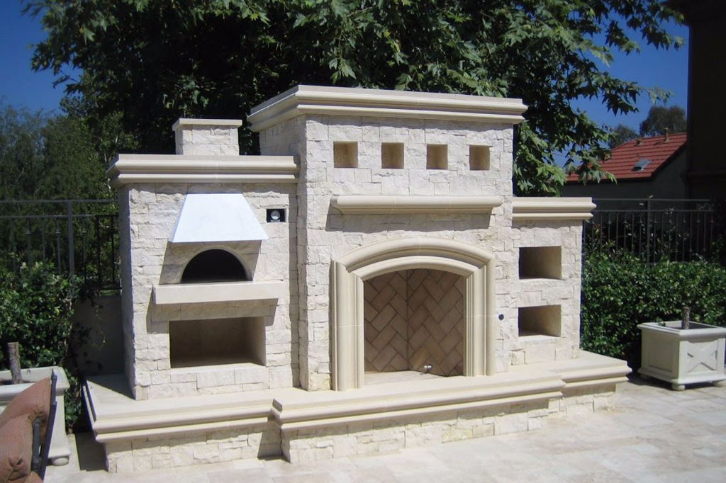 Limestone outdoor fireplace with an arched firebox and a domed pizza oven built into the same structure, on a raised travertine hearth