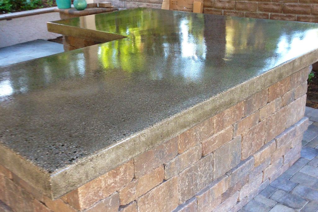Long outdoor bar counter cast in concrete with exposed aggregate, set on a stacked stone base