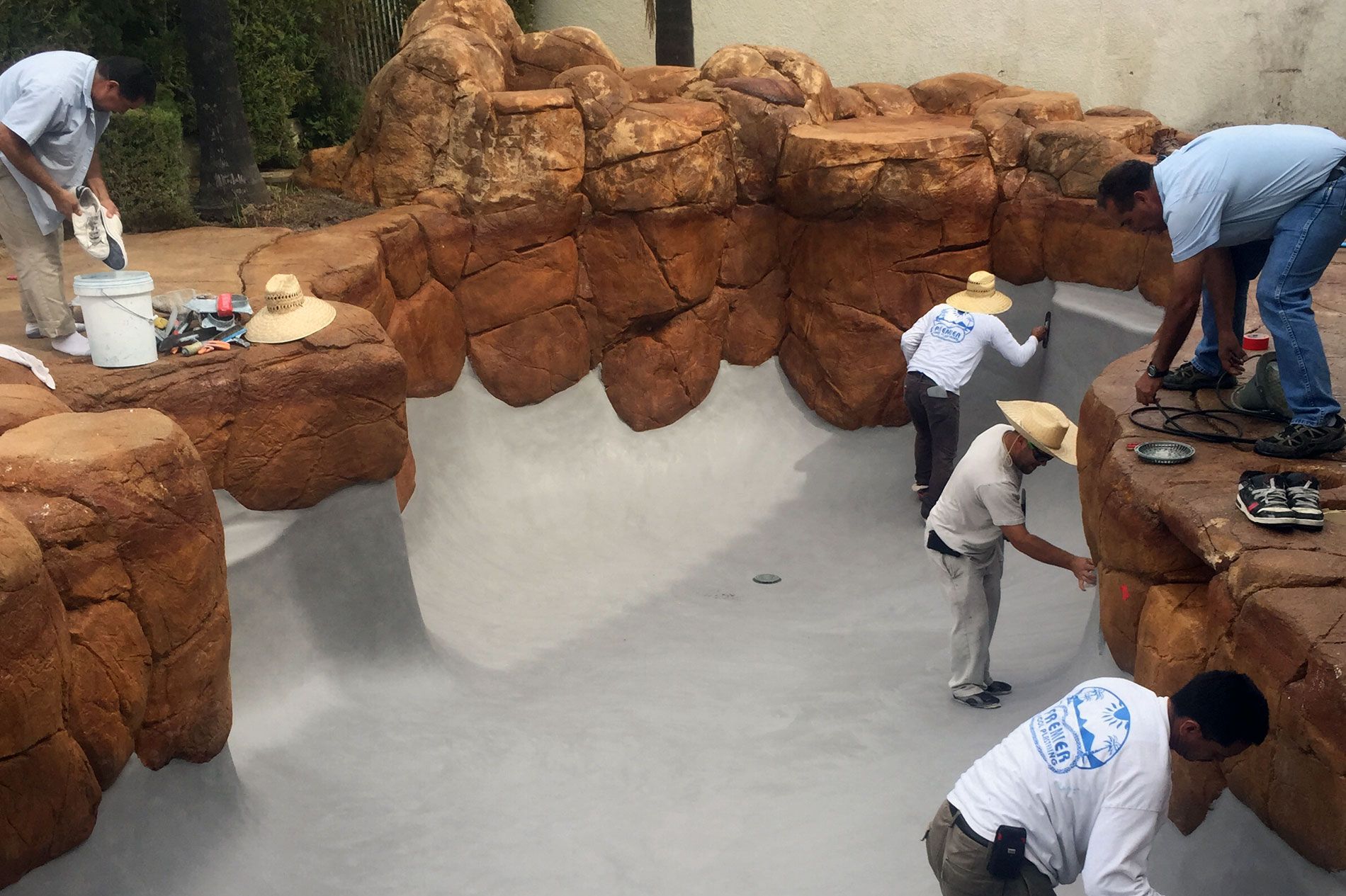 Crew finishing a pool shell with artificial rock coping built up around the waterline