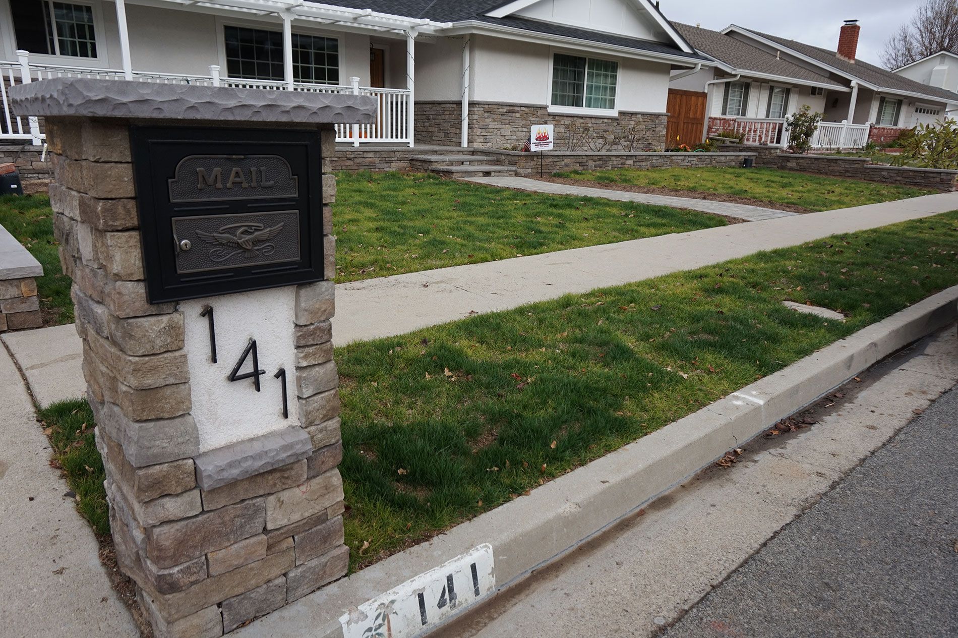 Stone veneer mailbox pillar with a slate cap and house numbers, built to match the home behind it