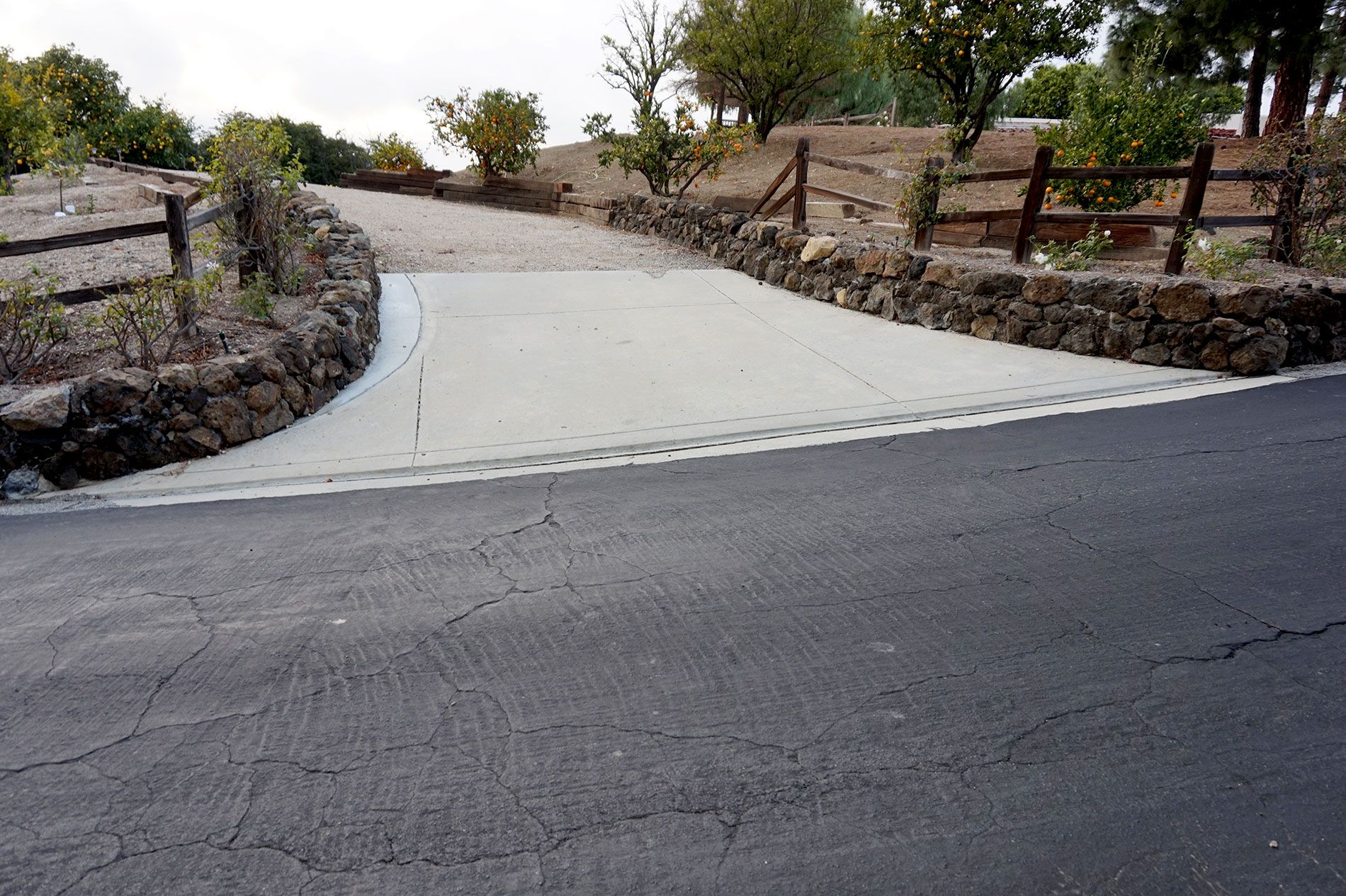 Long concrete driveway climbing a hillside lot between stacked stone retaining walls