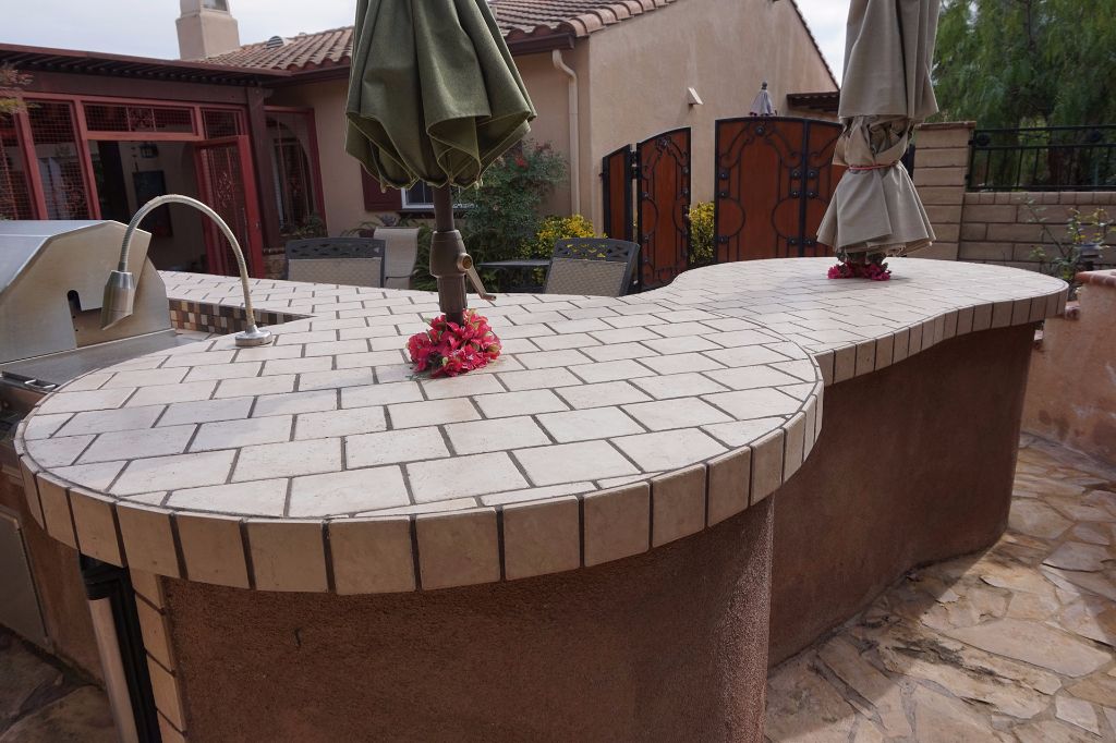Outdoor kitchen counter curving back toward the house, with shade umbrellas over the tiled bar top