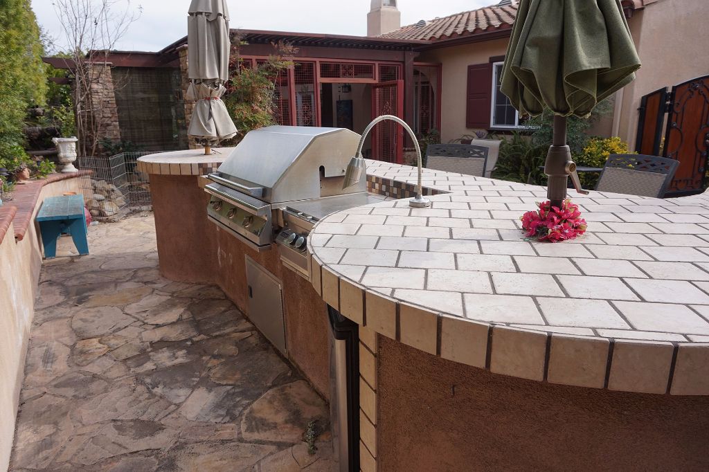 Curved outdoor kitchen with a tiled counter, built-in gas barbecue and stainless sink on a flagstone patio