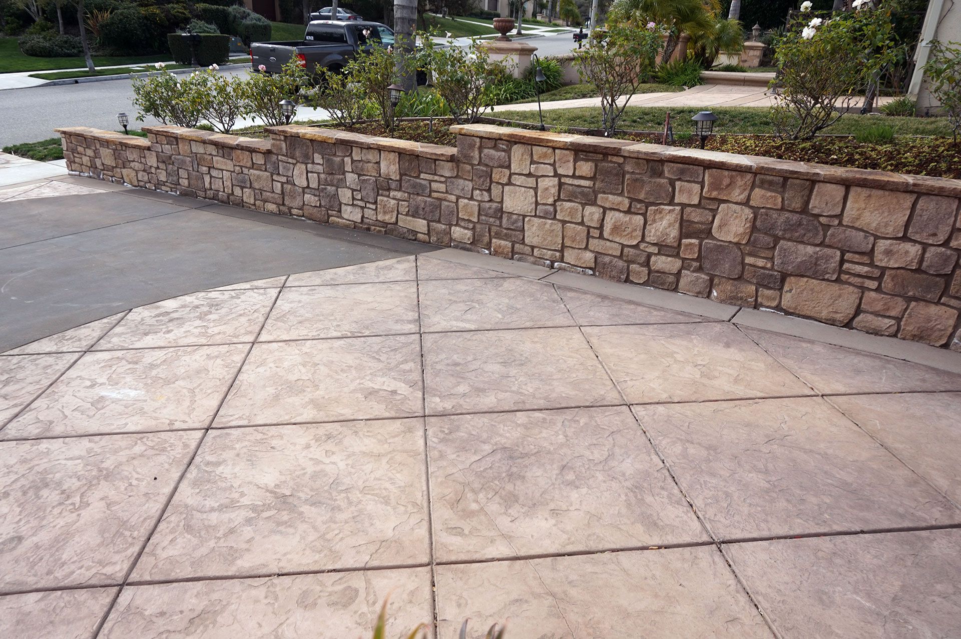 Stone-faced retaining wall curving alongside a stamped concrete driveway at a Dos Vientos property in Newbury Park