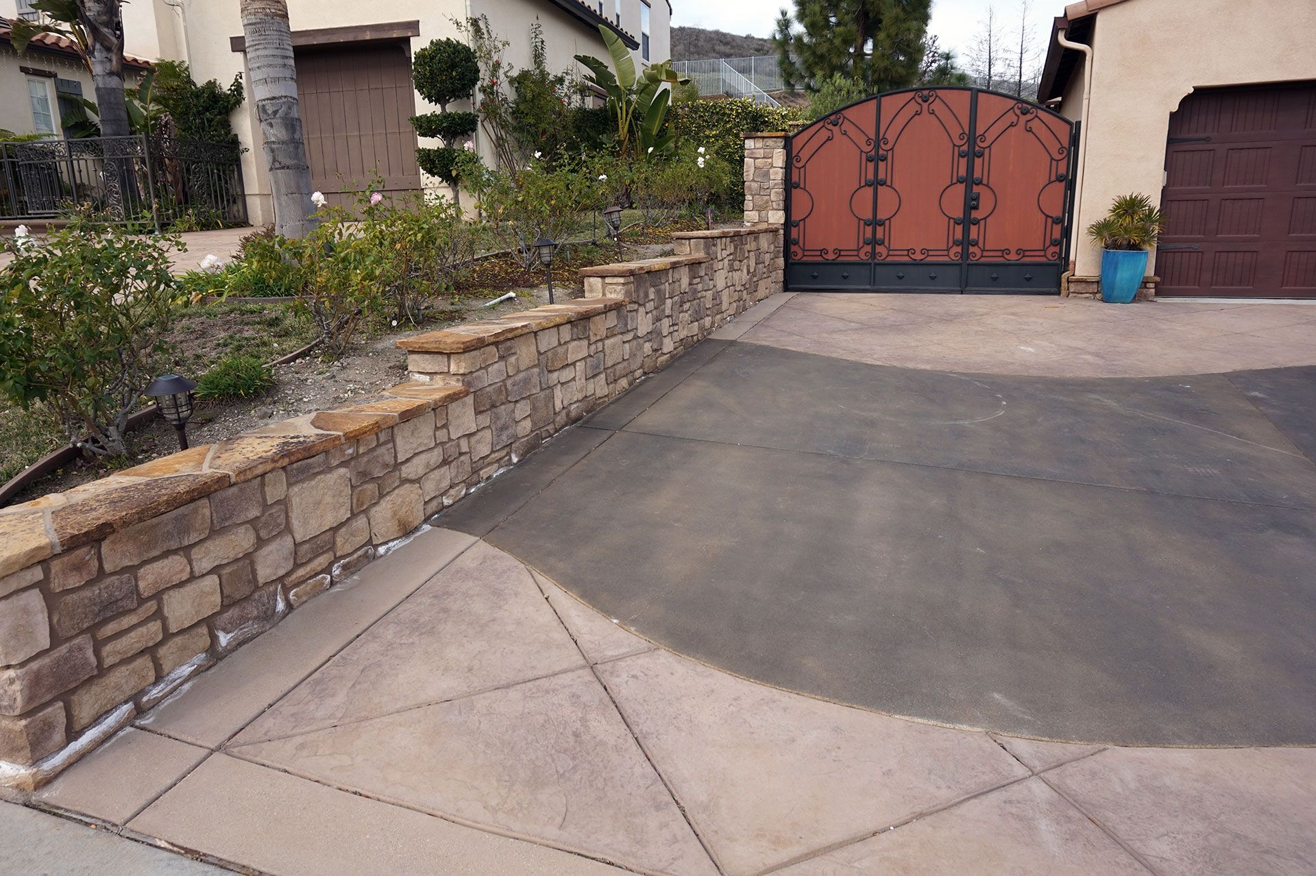 Stacked stone property-line retaining wall beside a broad concrete driveway at a Dos Vientos home