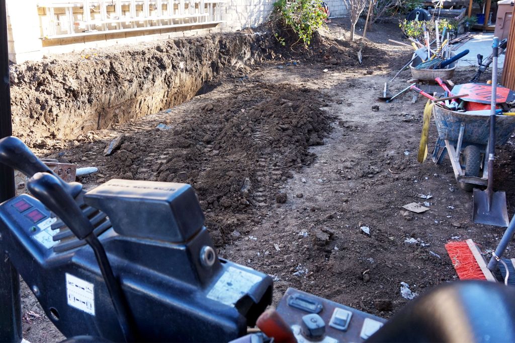 Excavated cut for a retaining wall footing, seen from the operator seat