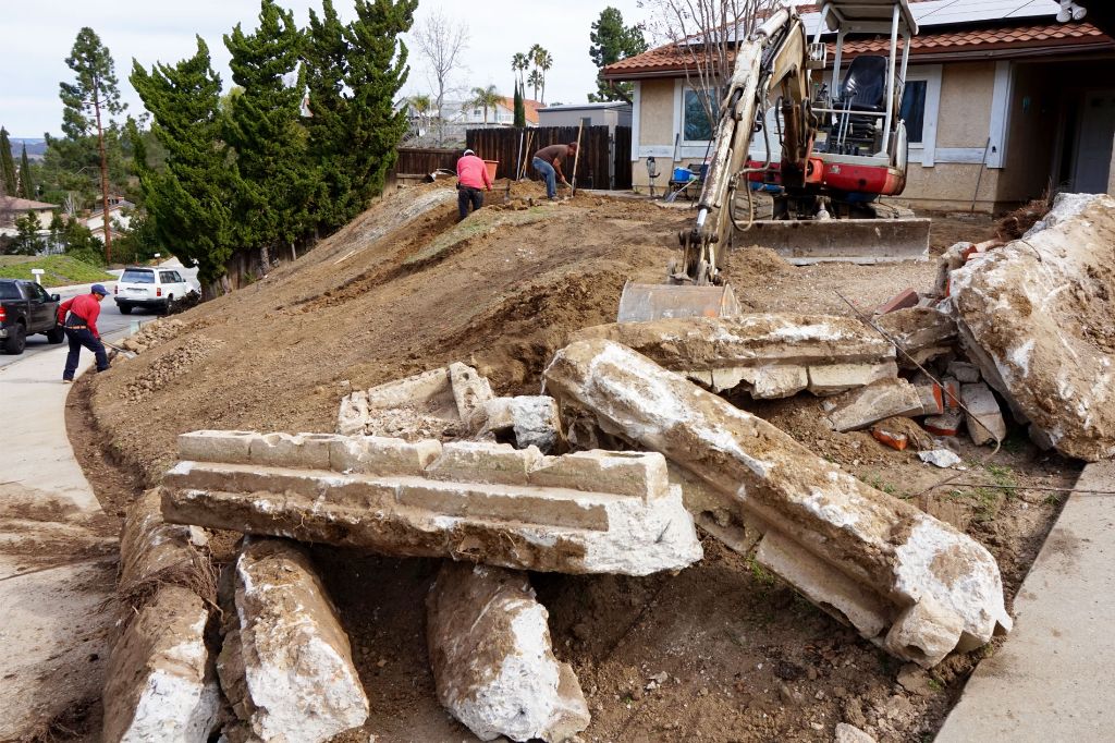 Excavator lifting out broken concrete slabs during a front-yard removal