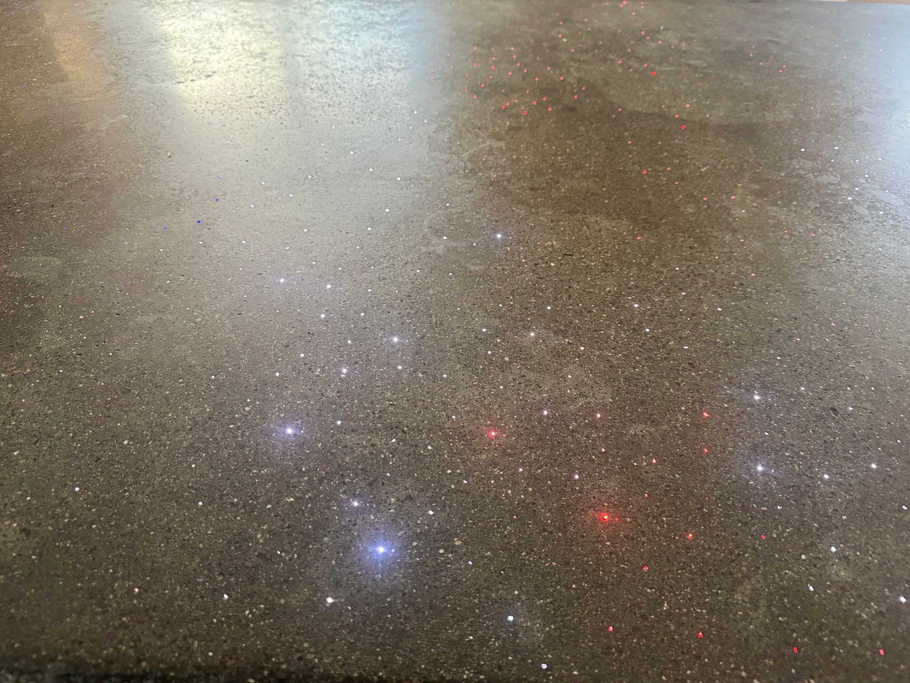 Close on the polished concrete surface in daylight, exposed aggregate and lit fiber ends sitting flush in the finish