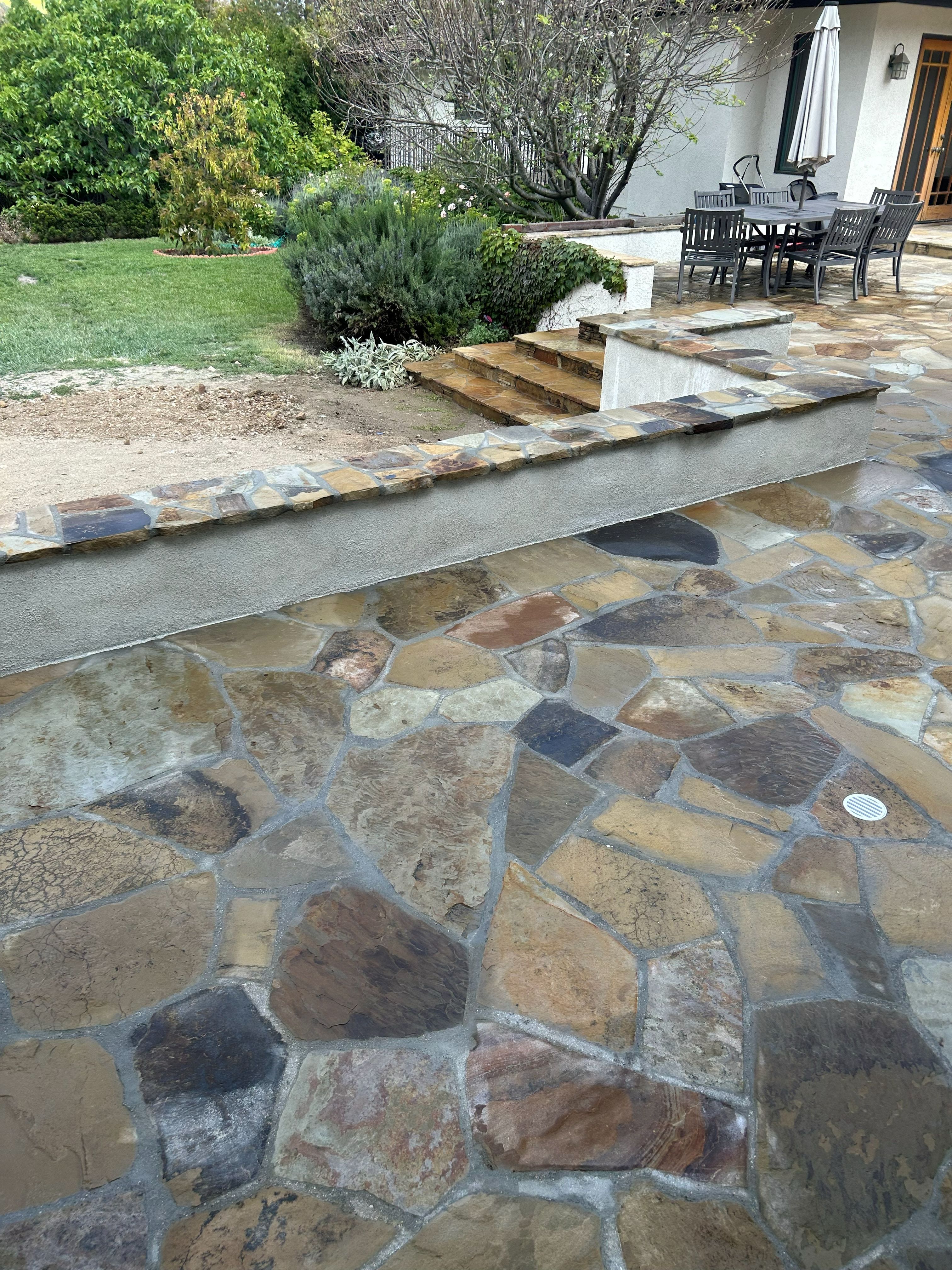 Flagstone patio across a back garden with dining furniture and mature planting