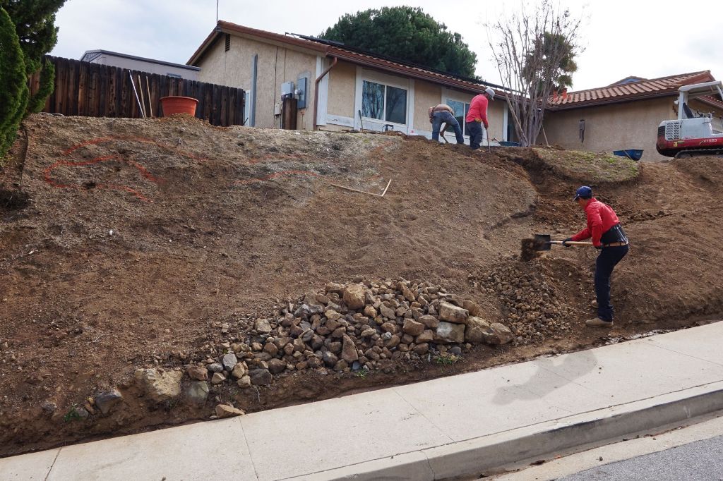 Crew hand-finishing a graded slope with a cobble drainage course along its base