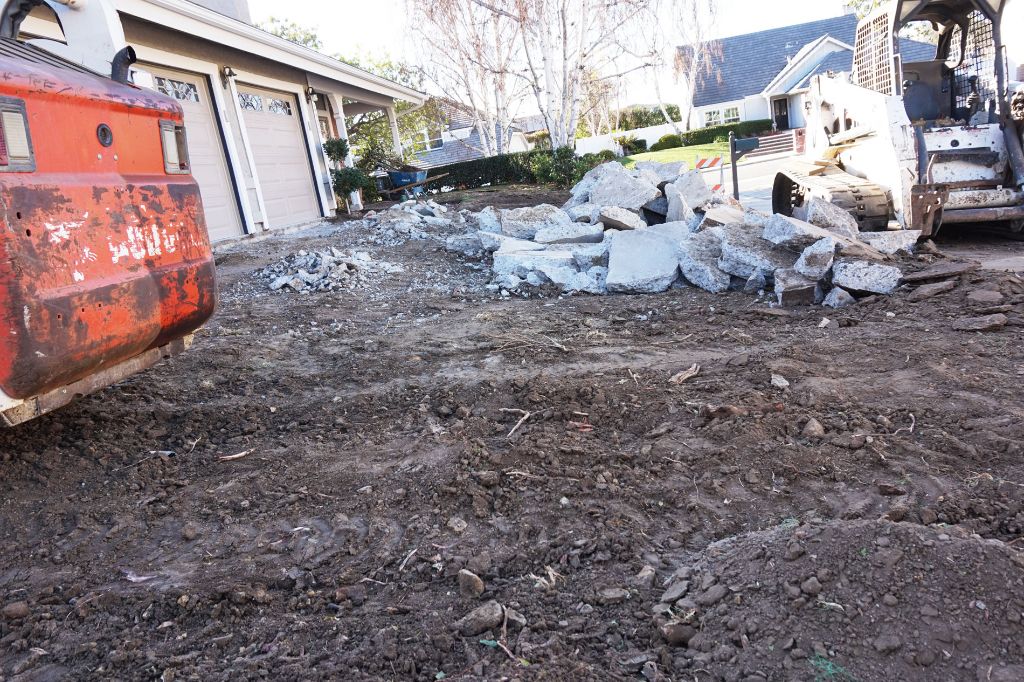 Demolished concrete and graded subgrade in front of a three-car garage, ready for a new pour