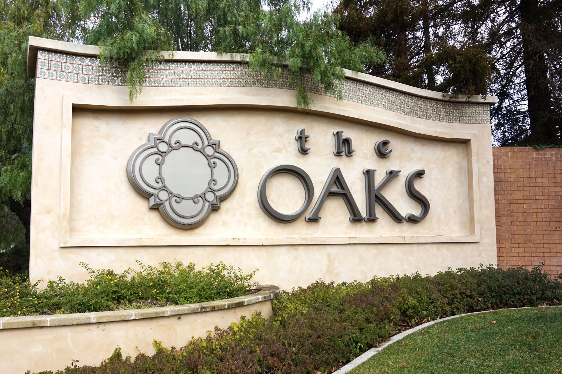 Stone and stucco monument sign reading "The Oaks" set into a landscaped bed