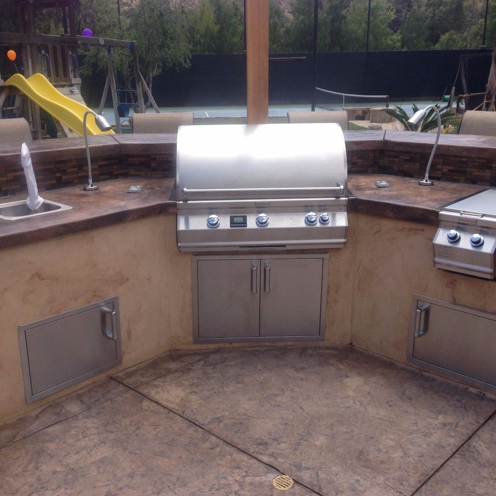 Outdoor kitchen wrapped around a stamped concrete patio, acid-stained concrete counter with a mosaic tile band and built-in grill