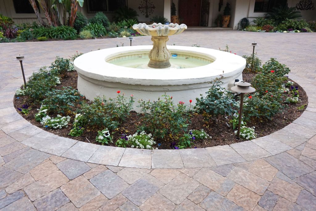 Circular tiered fountain set into a paver surround with planted beds