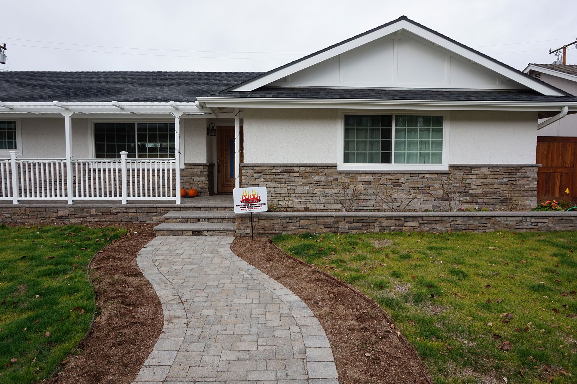 Curving paver walkway crossing the front lawn to a ranch house skirted in stone veneer