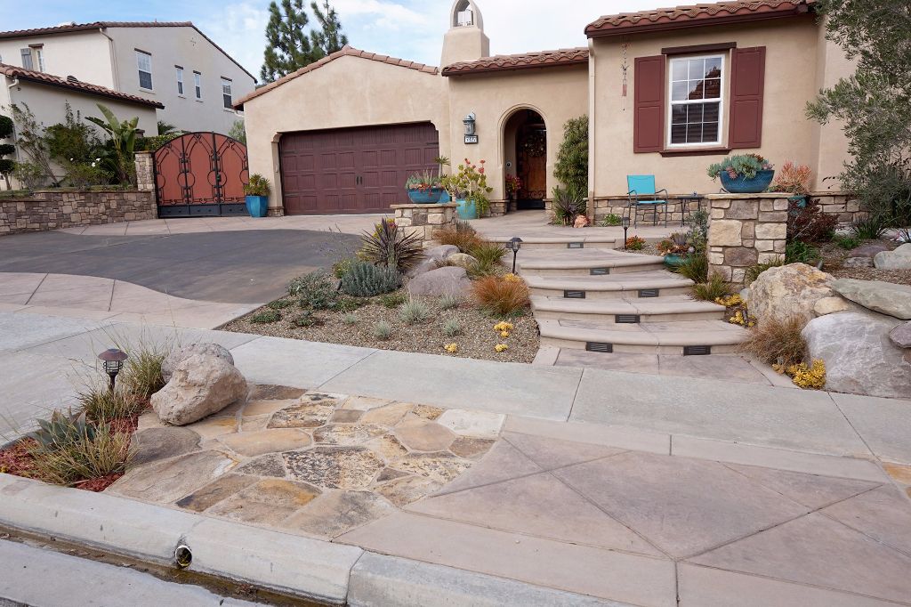 Flagstone panels set into the sidewalk and concrete steps rising to the entry, between stone walls and drought planting