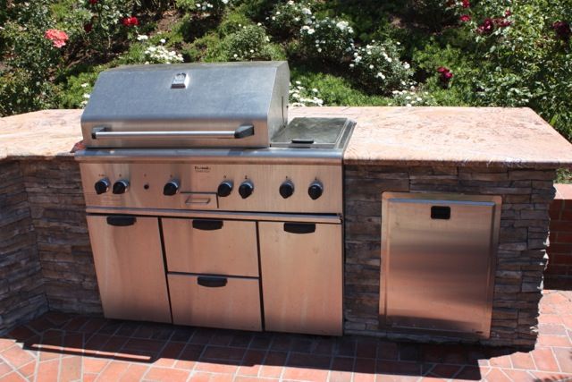 Stacked stone barbecue island with a stone counter and stainless grill, set on a brick paver patio