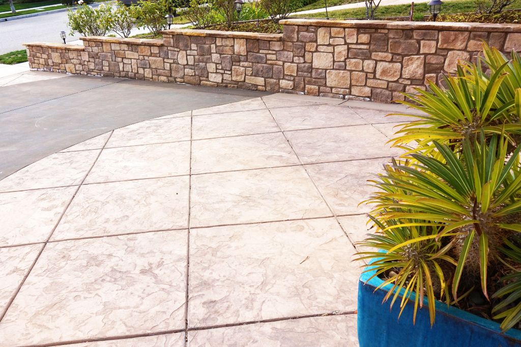Broad stamped concrete driveway laid out in saw-cut panels, edged by a stone retaining wall with a cut cap
