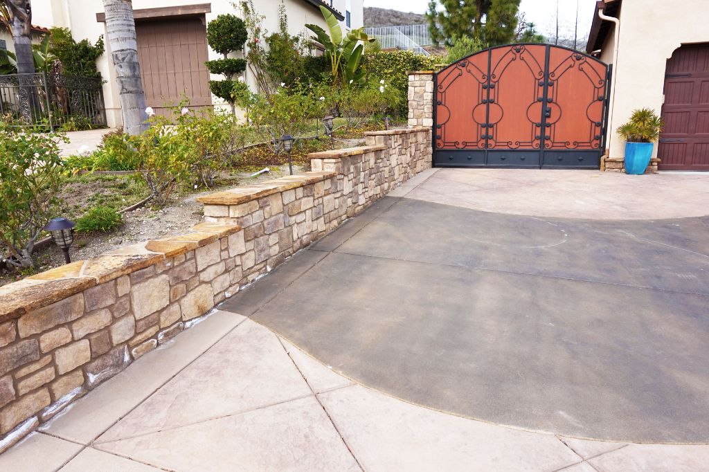 Driveway climbing to an iron gate between stacked stone retaining walls on a Spanish-style property