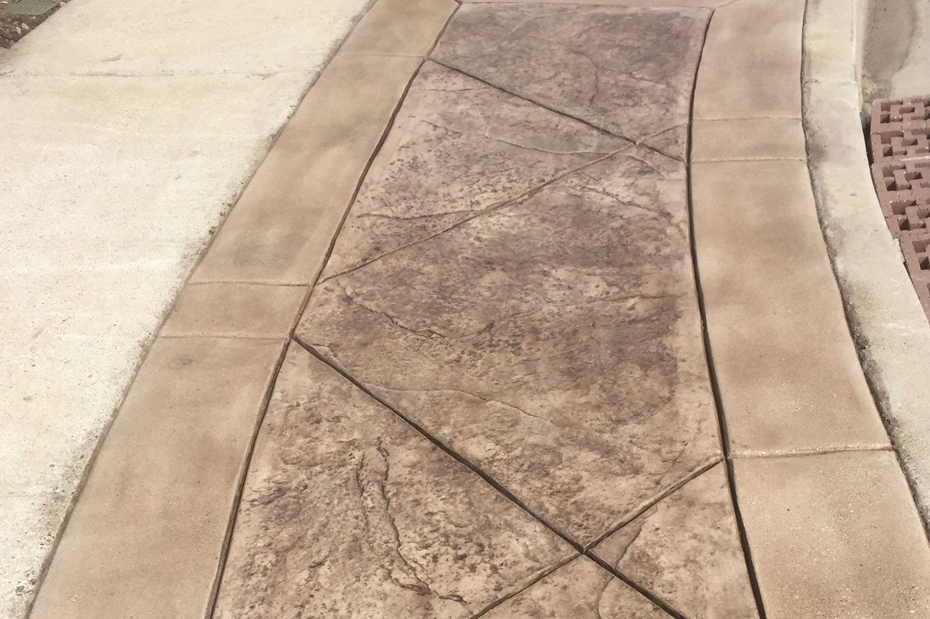 Freshly stamped concrete walkway in a tan ashlar pattern, the curved border banding scored in before the slab cured
