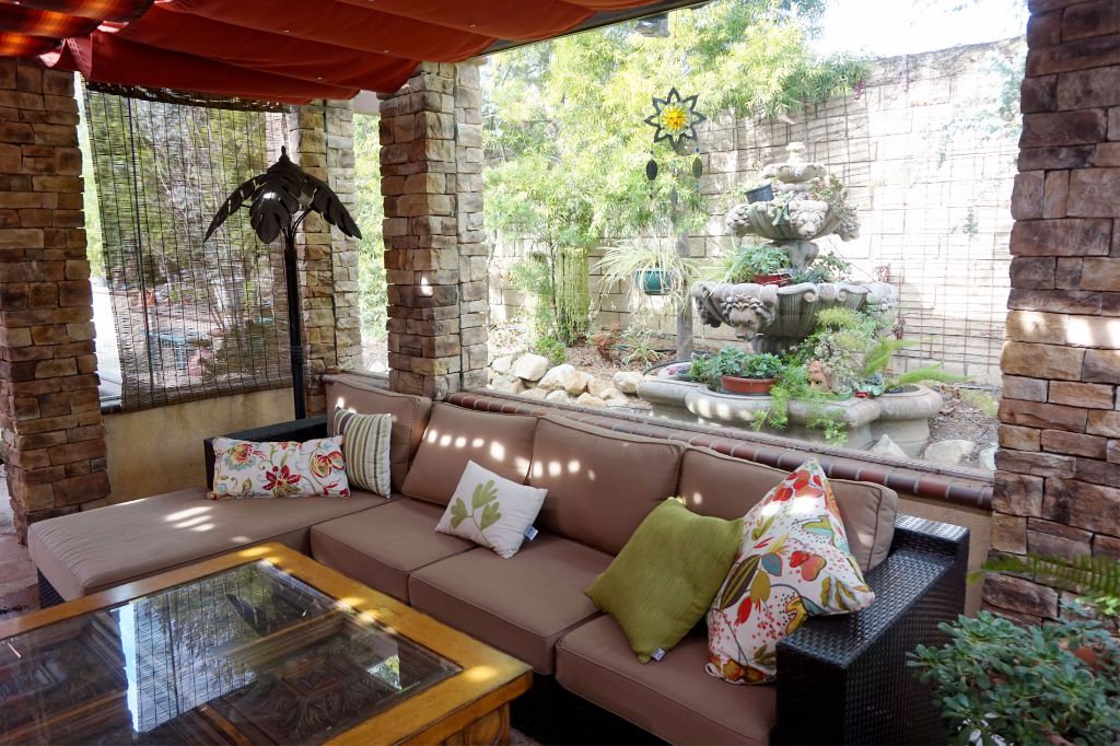 Stacked stone columns carrying a covered outdoor living room, looking out past a tiered stone fountain