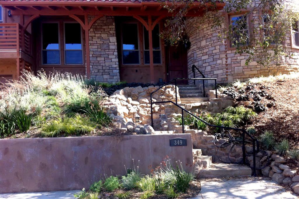 Stone veneer frontage with a stepped entry, iron handrail and a boulder water feature set into the planting