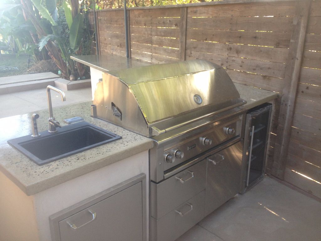 Stucco outdoor kitchen with a stainless built-in grill, undercounter fridge and a sink set into a speckled stone counter