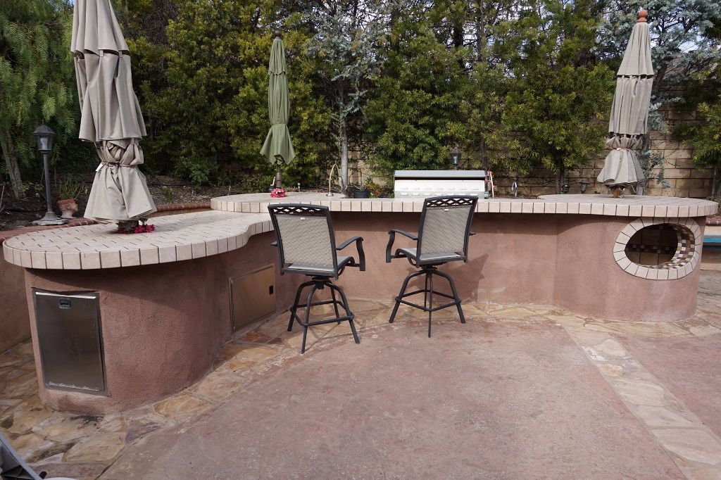 Curved outdoor kitchen counter in tile and stucco with a built-in pizza oven, bar seating and a flagstone patio