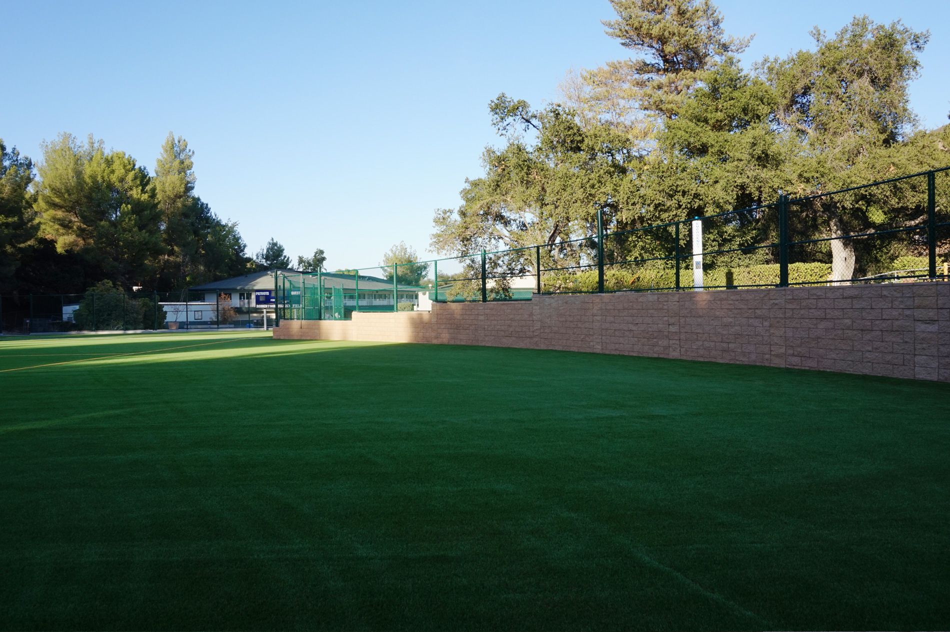 Block outfield wall running the boundary of the Viewpoint School field, capped and rendered