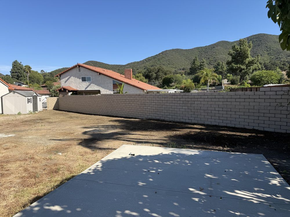Tan block wall built on the old fence line, the same concrete slab in the foreground and the hills beyond