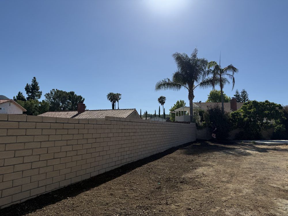 Long block wall running the length of a bare dirt yard