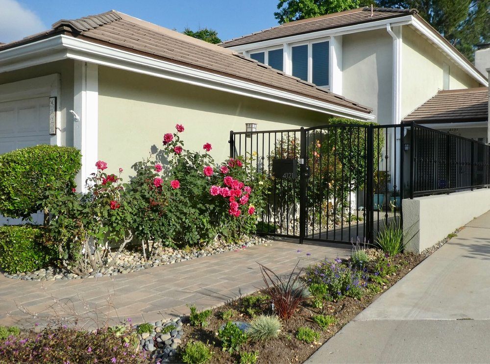 Front of a Conejo Valley home with rose beds, a black metal fence and a paved drive