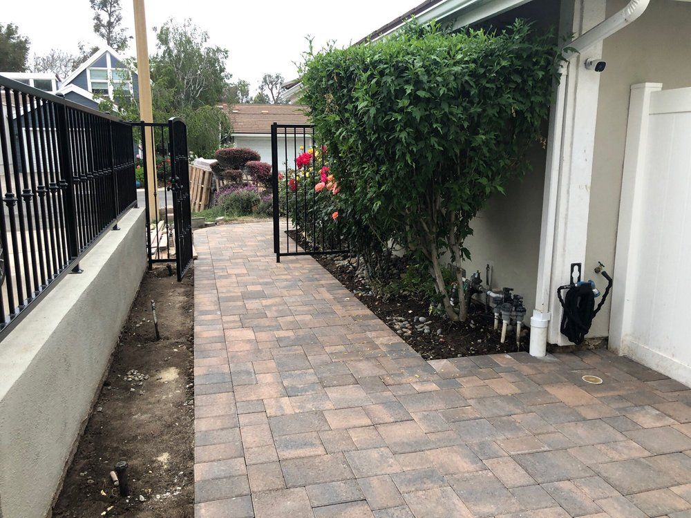 Paver walkway with a black metal fence and a clipped hedge