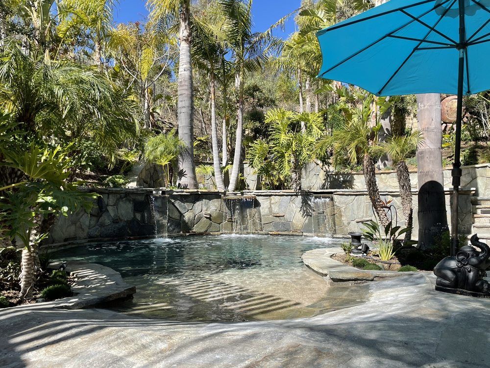 Swimming pool with a raised stone water feature, palms and a blue market umbrella