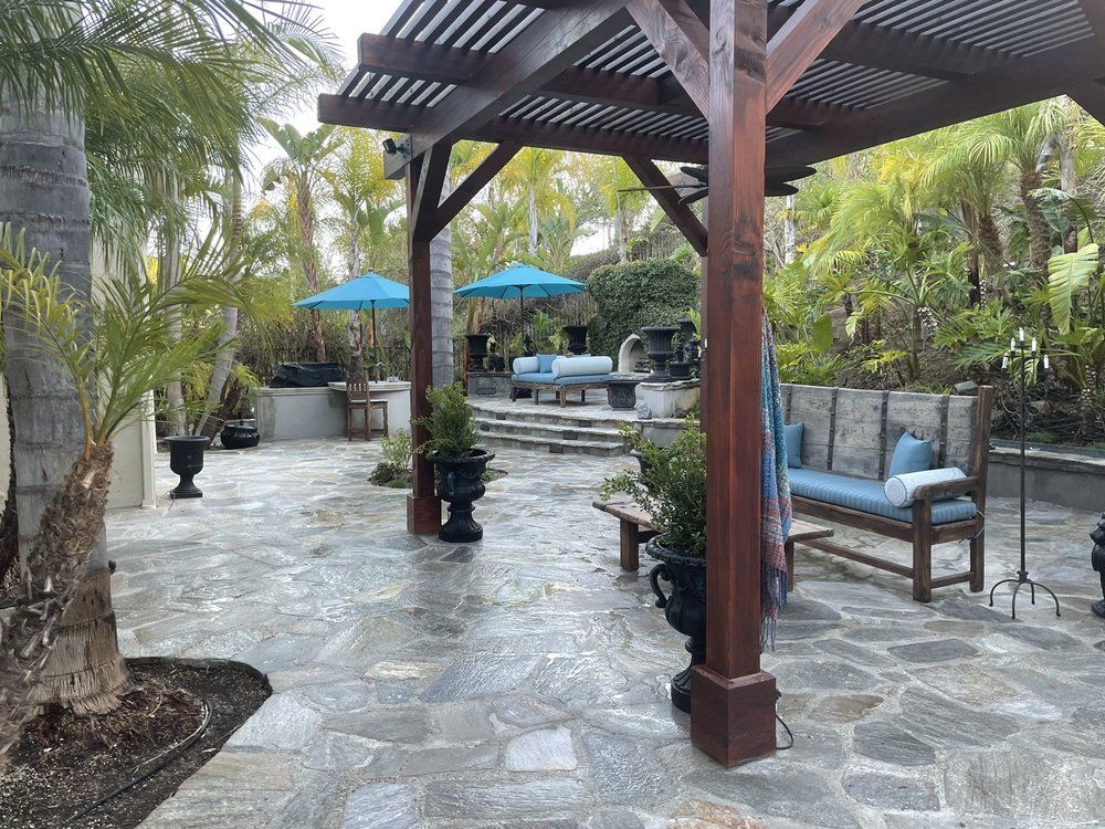 Natural stone patio under a timber pergola with blue umbrellas and lounge seating