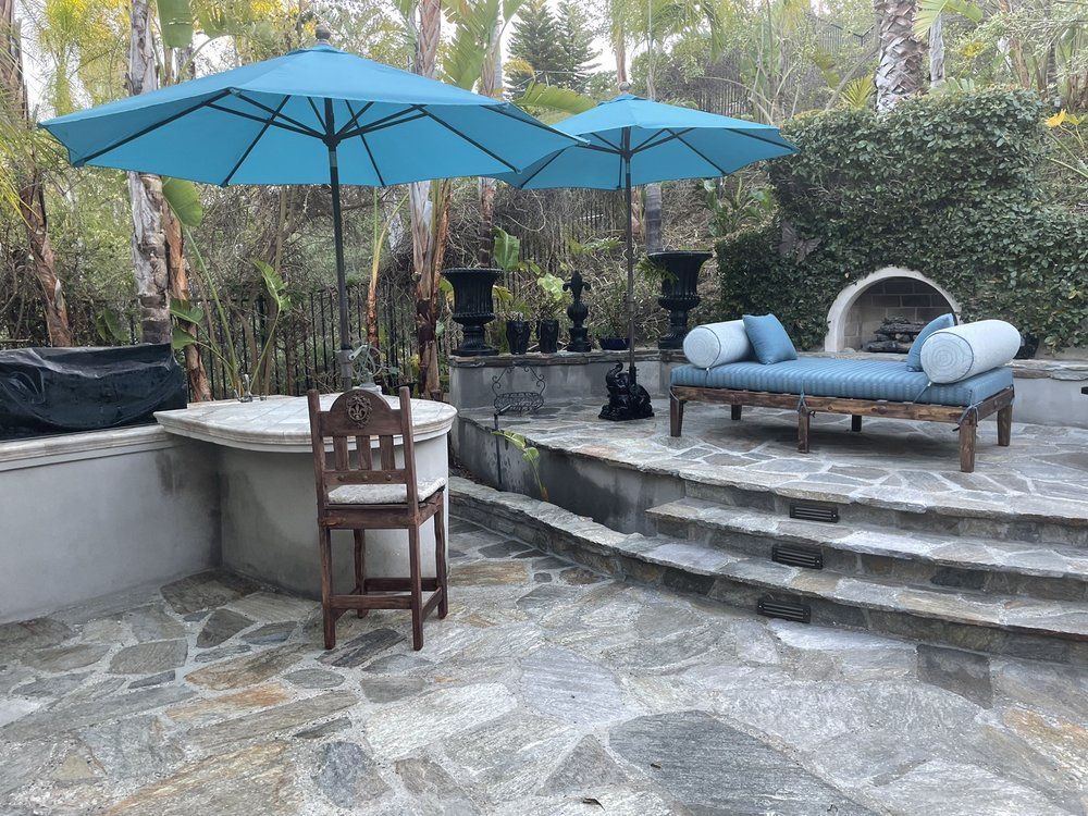 Natural stone patio and steps with blue umbrellas beside a raised planter